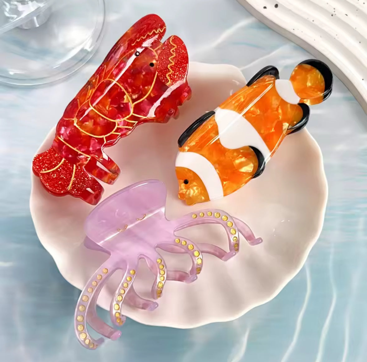 Pince à cheveux en forme de poisson clown orange et blanc posée sur une assiette nacrée