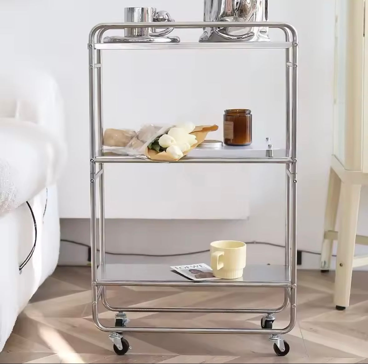 Desserte inox 3 niveaux avec bougie et livres placée près d’un canapé moderne