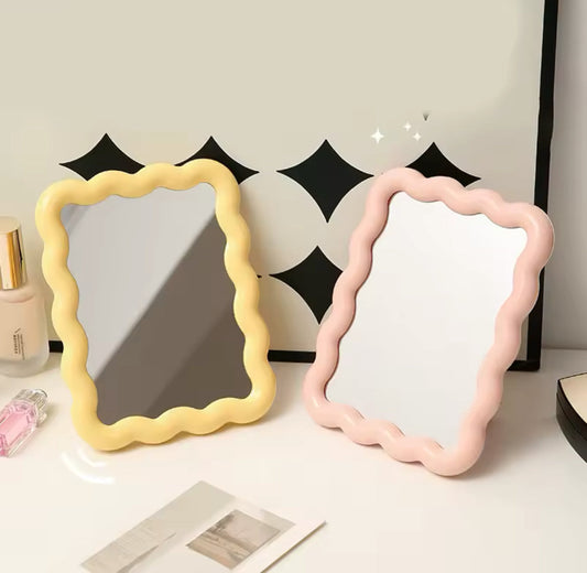 Miroirs ondulés jaunes et roses posés sur table blanche, déco pastel