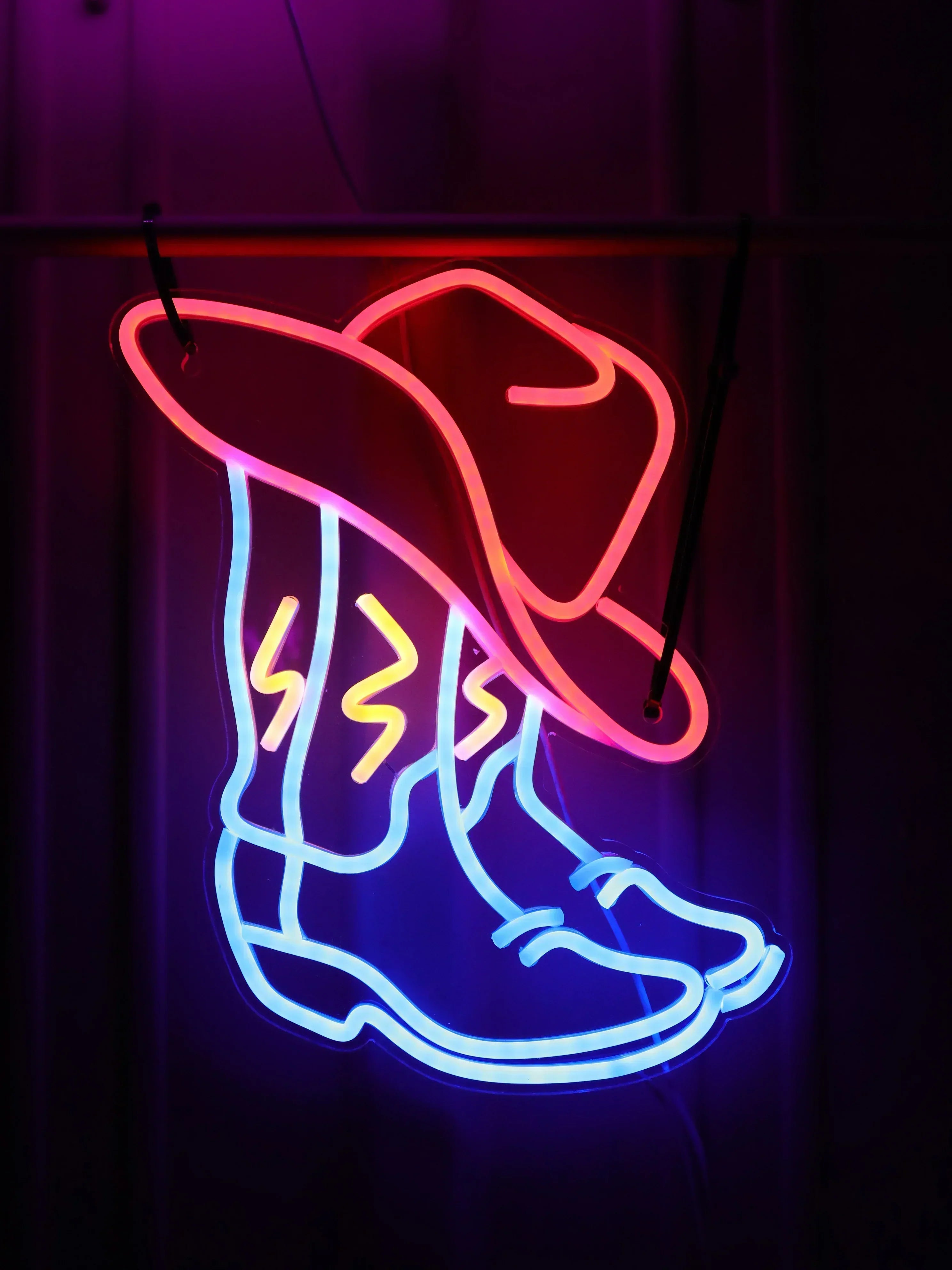 Néon Santiag LED inspiré du style cowboy popularisé par Beyoncé, bottes et chapeau lumineux sur mur en bois.